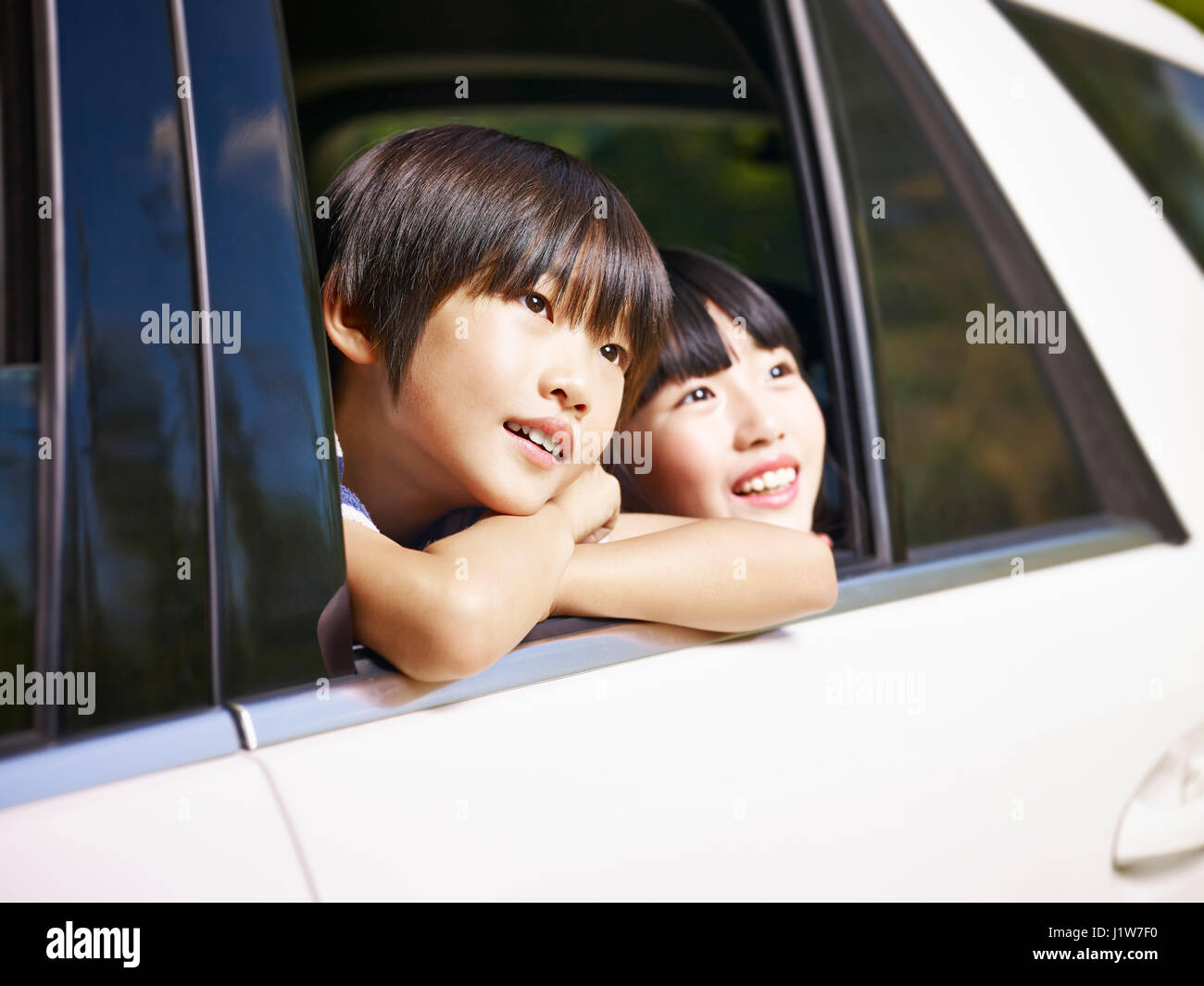 Felices los niños asiáticos pegando su cabeza fuera de la ventana trasera de un coche, mirando el paisaje. Foto de stock