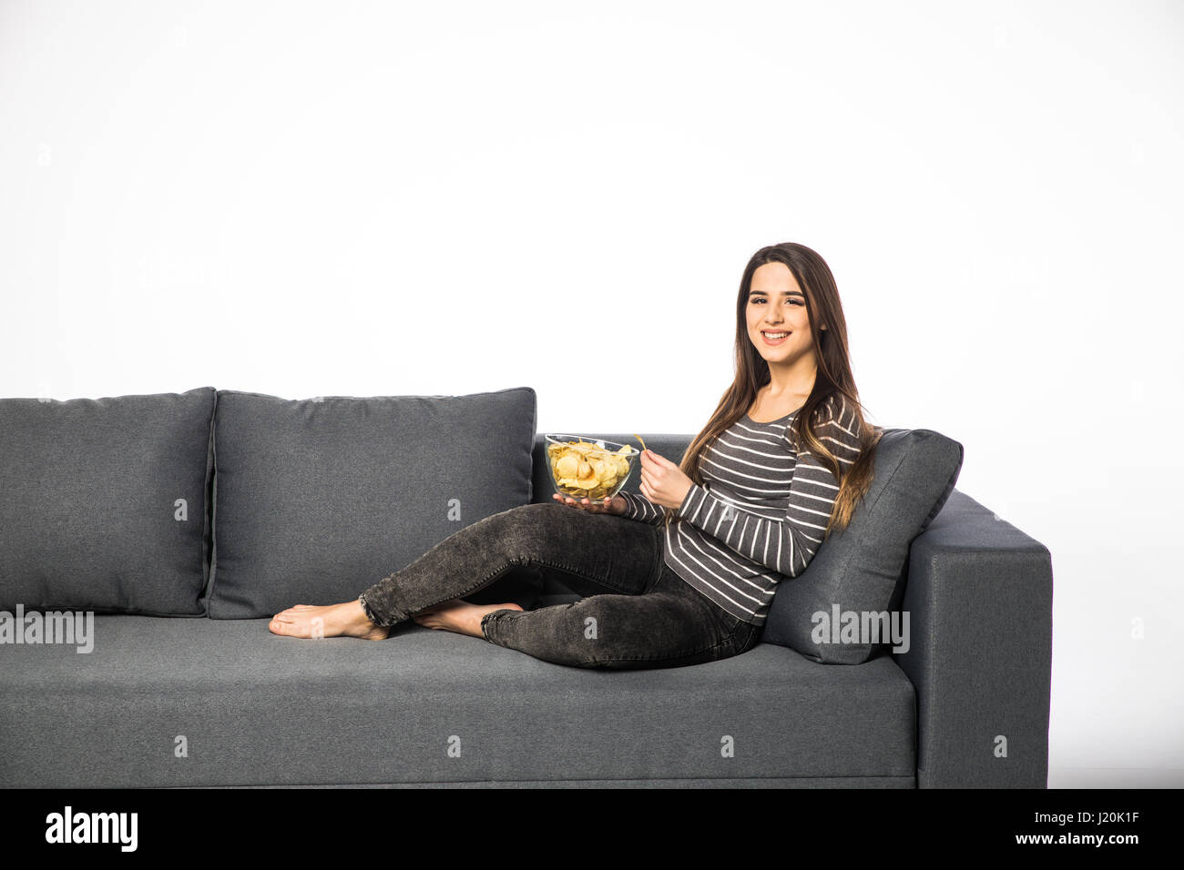 Hermosa chica interna comiendo patatas fritas, viendo la televisión,  sentado en el sofá Fotografía de stock - Alamy