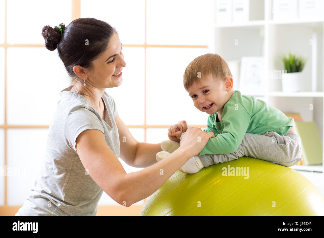 Madre solícita haciendo ejercicios deportivos con su niño sobre fitball Foto de stock