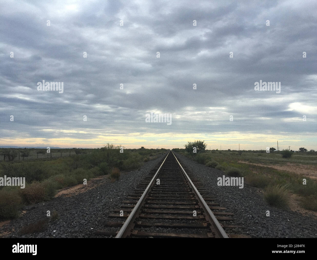 Perspectiva decreciente de vía férrea contra el cielo nublado durante la puesta de sol Foto de stock