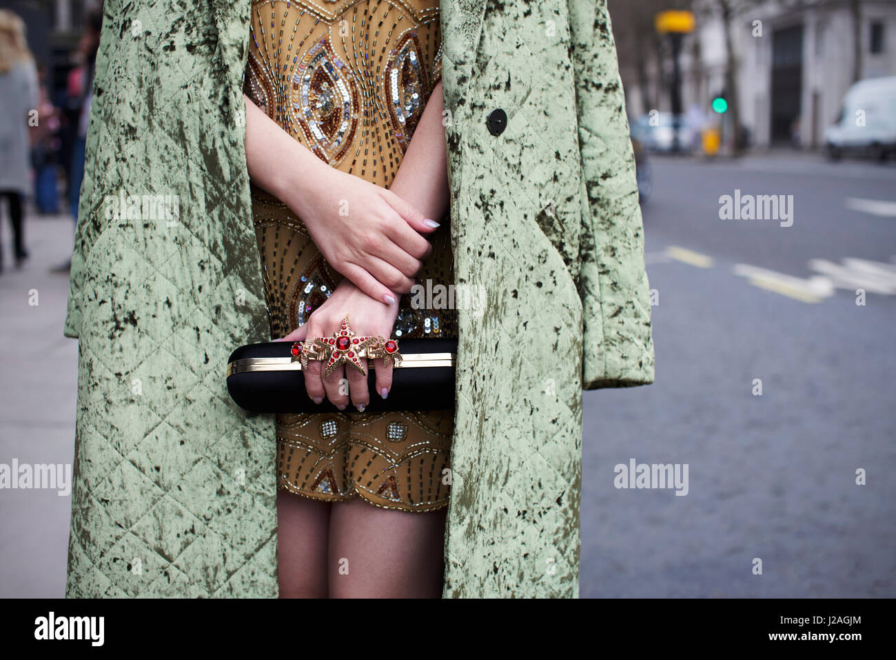 Londres - Febrero, 2017: sección intermedia de moda mujer vestidos de verde a través de una capa de terciopelo aplastado minidress con abalorios y anillos grandes, de pie en la calle durante la Semana de la Moda de Londres, horizontal Foto de stock