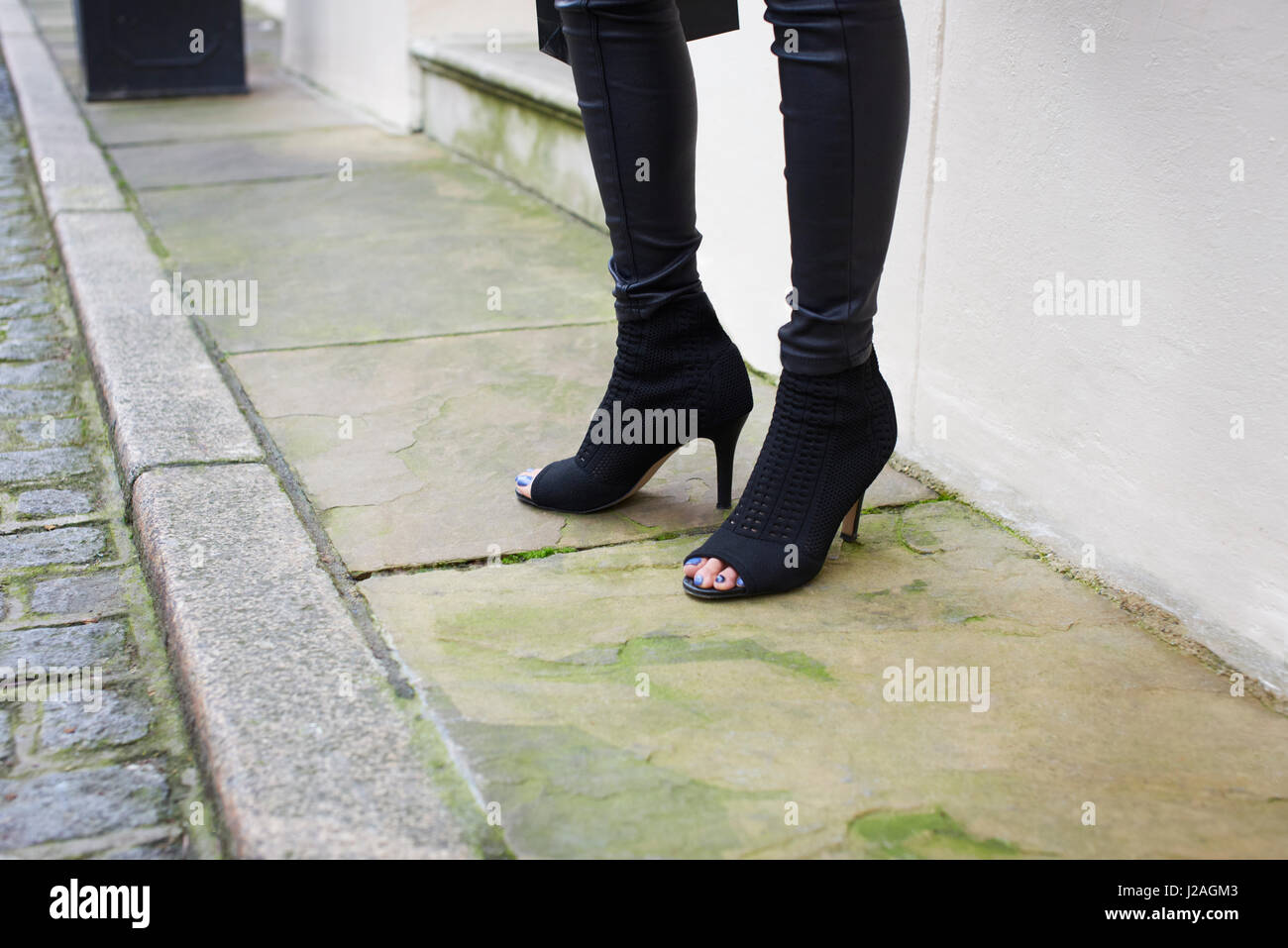 Londres - Febrero, 2017: Bajo la sección de Mujer de pie en una calle vistiendo open toe Stiletto talón botines de gamuza negra y pantalón negro apretado durante la Semana de la Moda de Londres, horizontal Foto de stock