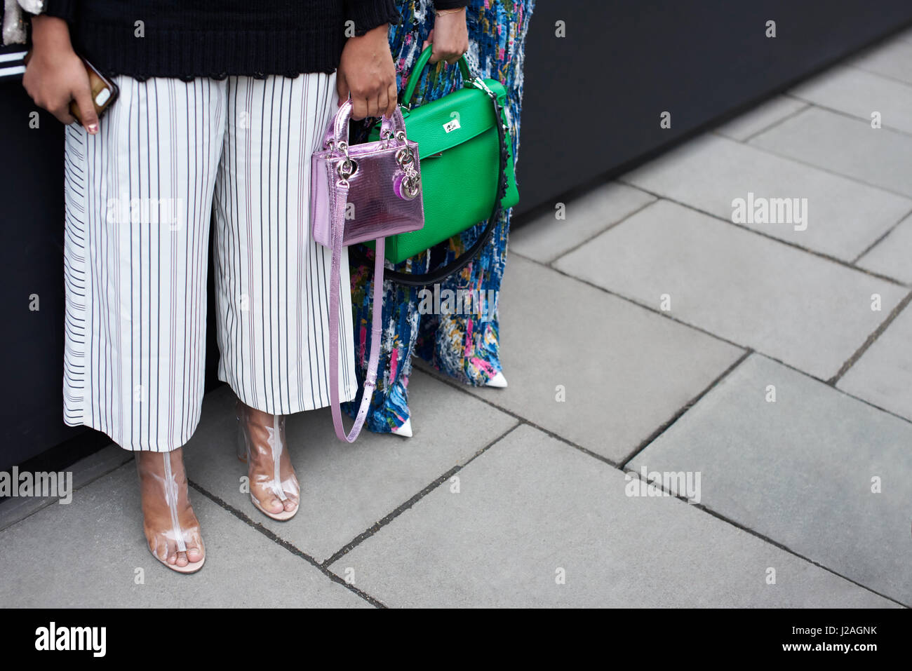 Londres - Febrero, 2017: Bajo la sección de dos mujeres de pie en una calle sosteniendo diseñador de bolsos de mano, un bolso de Hermes verde grande, y una pequeña bolsa de Dior metálicos, durante la Semana de la Moda de Londres, horizontal Foto de stock