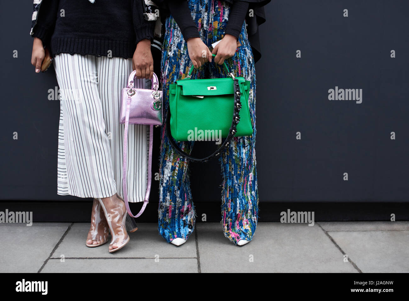 Londres - Febrero, 2017: Bajo la sección de dos mujeres de pie en una calle sosteniendo diseñador de bolsos de mano, un bolso de Hermes verde grande, y una pequeña bolsa de Dior metálicos, durante la Semana de la Moda de Londres, horizontal, vista frontal Foto de stock