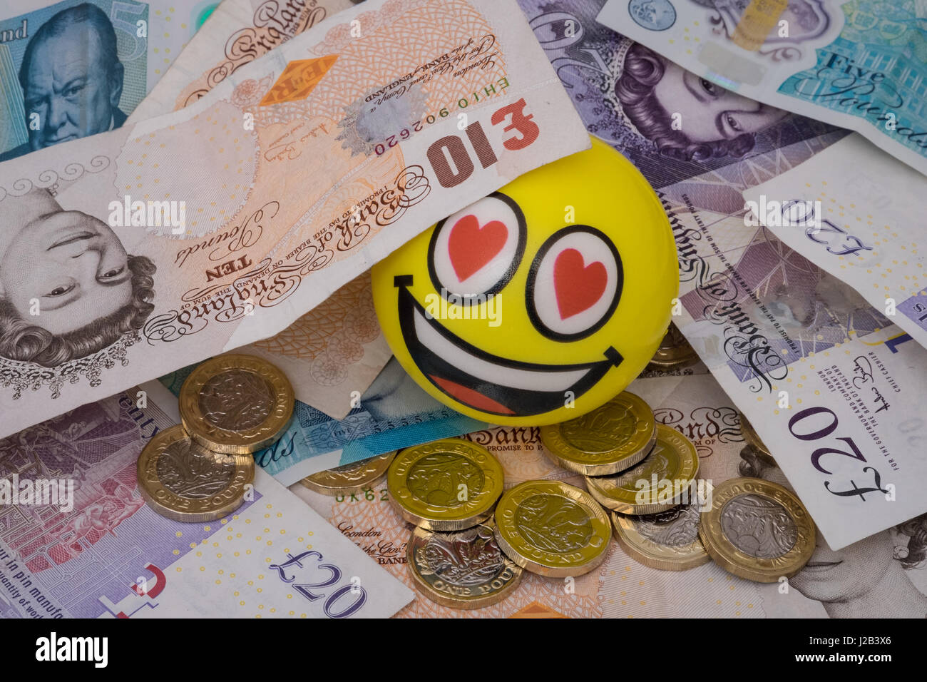 Emoji feliz con el rostro cubierto en uk dinero monedas y billetes Foto de stock