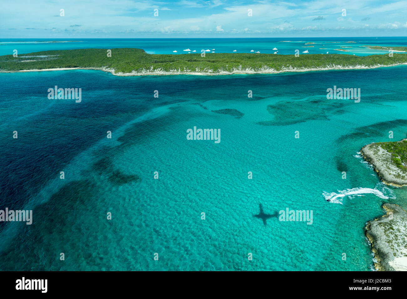 Foto aérea mirando hacia la sombra del avión, un jet ski y clara agua tropical y las islas de la cadena de islas de Exuma Bahamas cerca Staniel Cay. Foto de stock