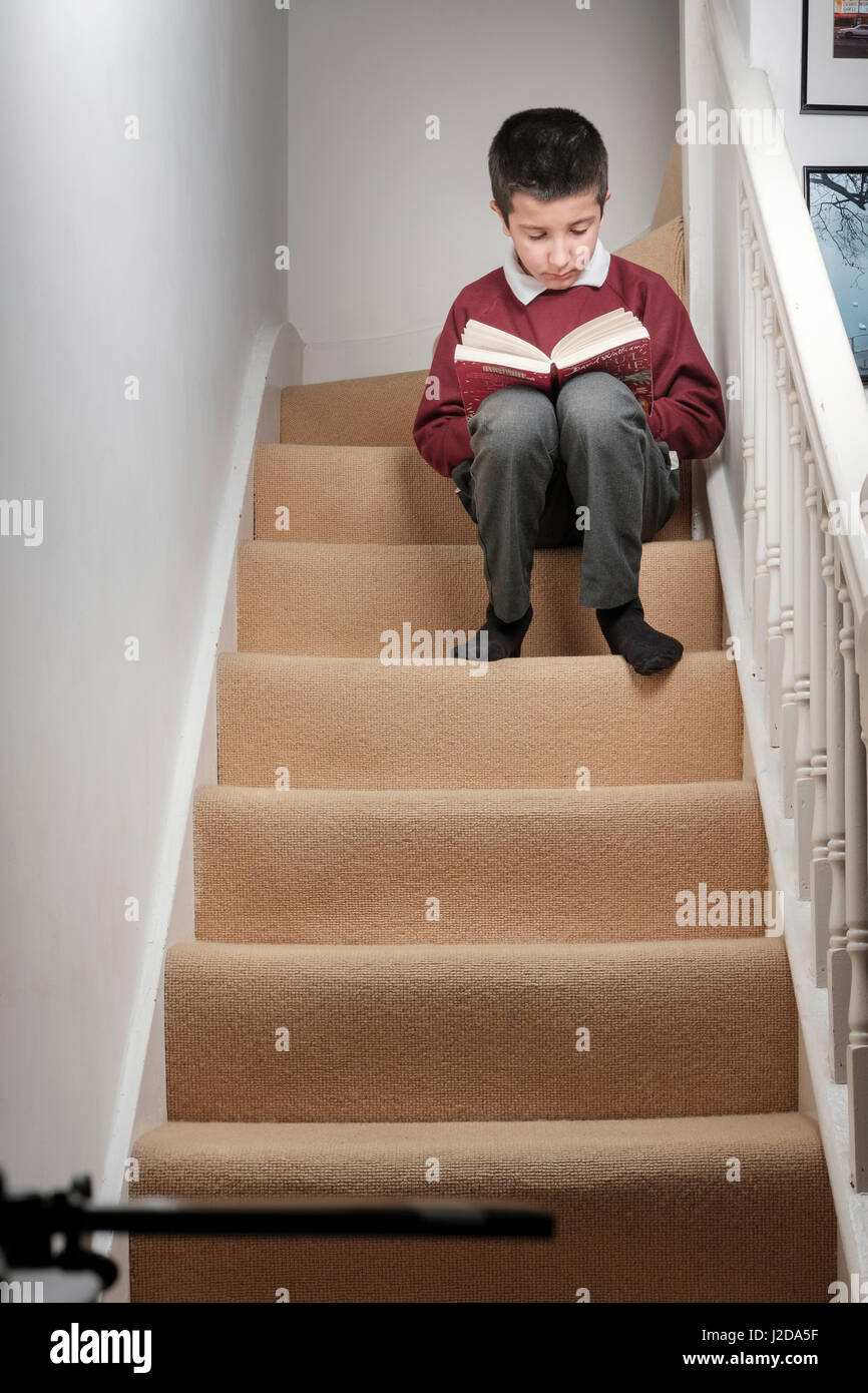 Londres,UK-colegial en uniforme escolar lee libro sentado en las escaleras en casa Foto de stock