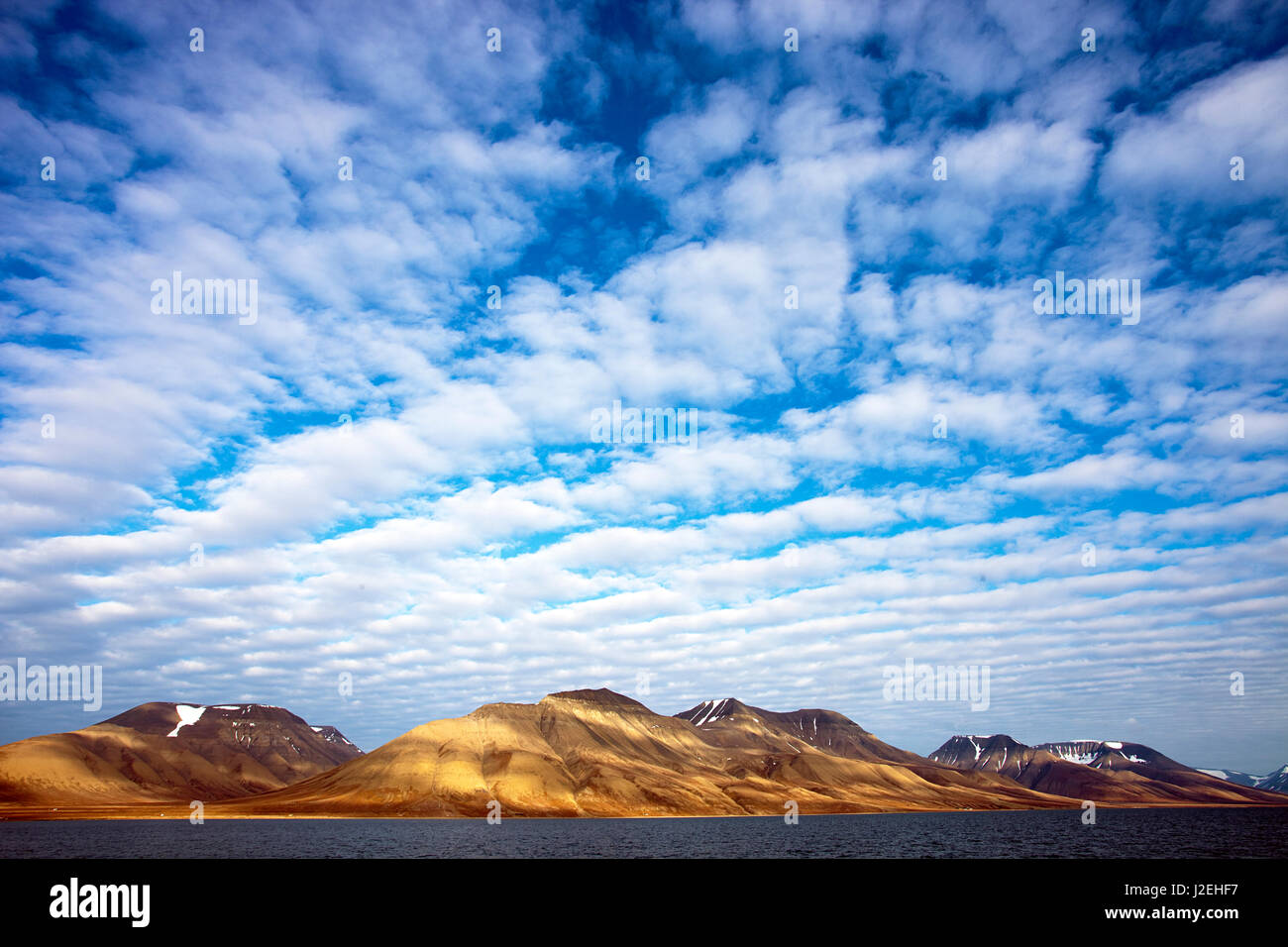 Ártico Svalbard, Isfjorden. Espina de Pez nubes dan lugar a un llamativo juego de luz sobre la tierra abajo. Foto de stock