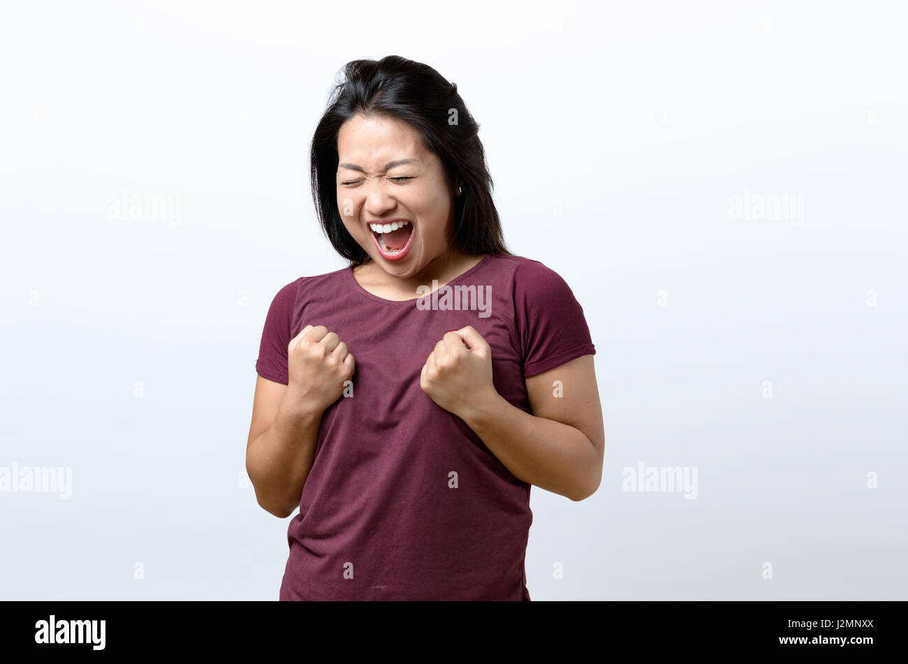 Exuberante joven China exultante animando una victoria, éxito o ganar golpeando el aire con sus puños y riendo sobre blanco con espacio de copia Foto de stock