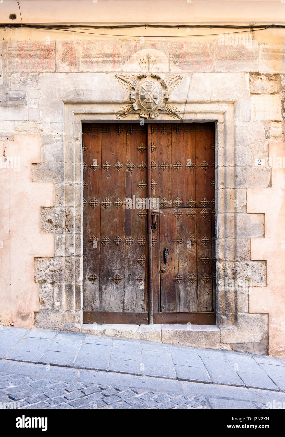 Dobles puertas antiguas de madera debajo de un escudo de armas en un edificio histórico en el casco antiguo de la ciudad medieval de Cuenca, Castilla La Mancha, España Foto de stock