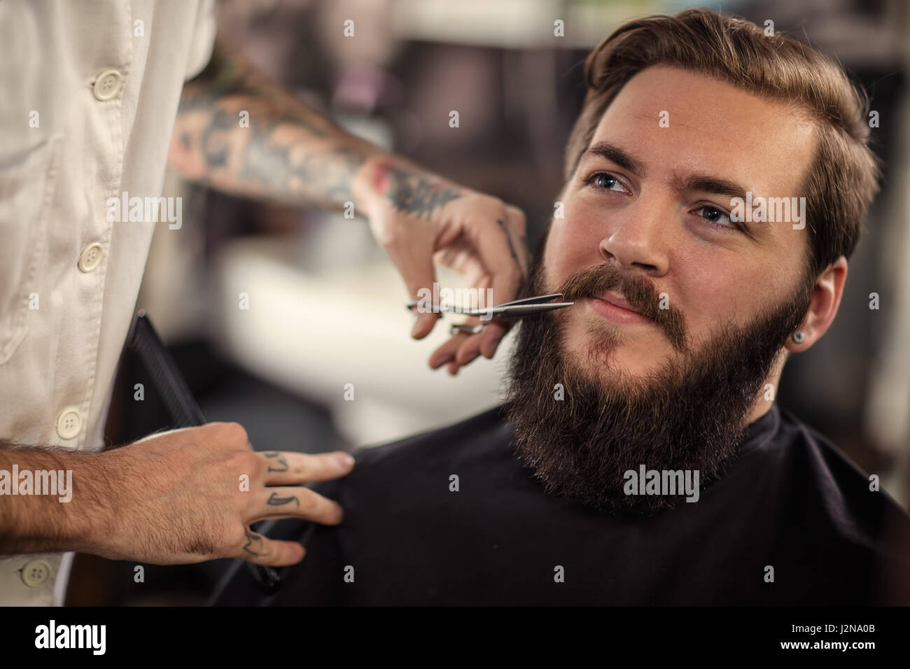 Hombre con tijeras de peluquería recortar el bigote cliente sonriente Foto de stock