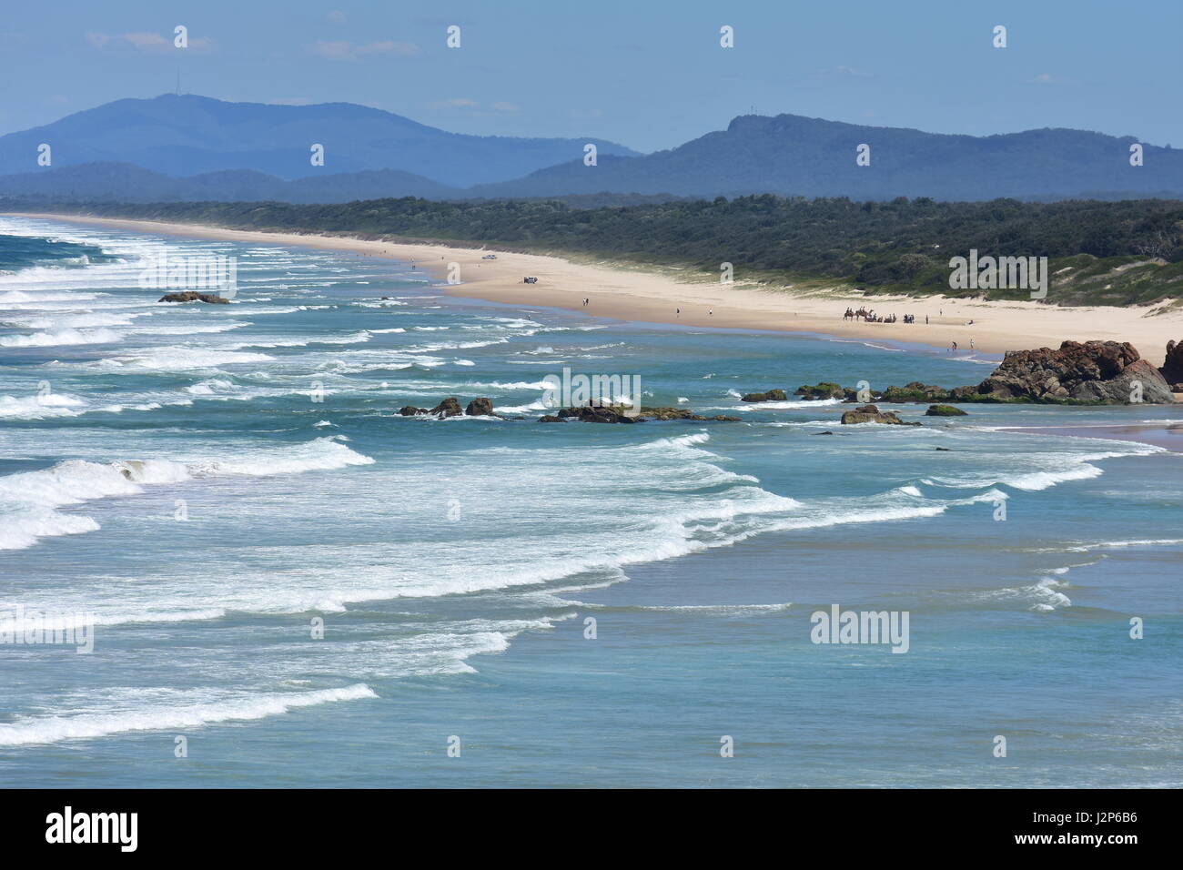 Playa de arena blanca con olas oceánicas rumbo al sur desde el punto Faro en Port Macquarie con tres hermanos en el fondo. Foto de stock