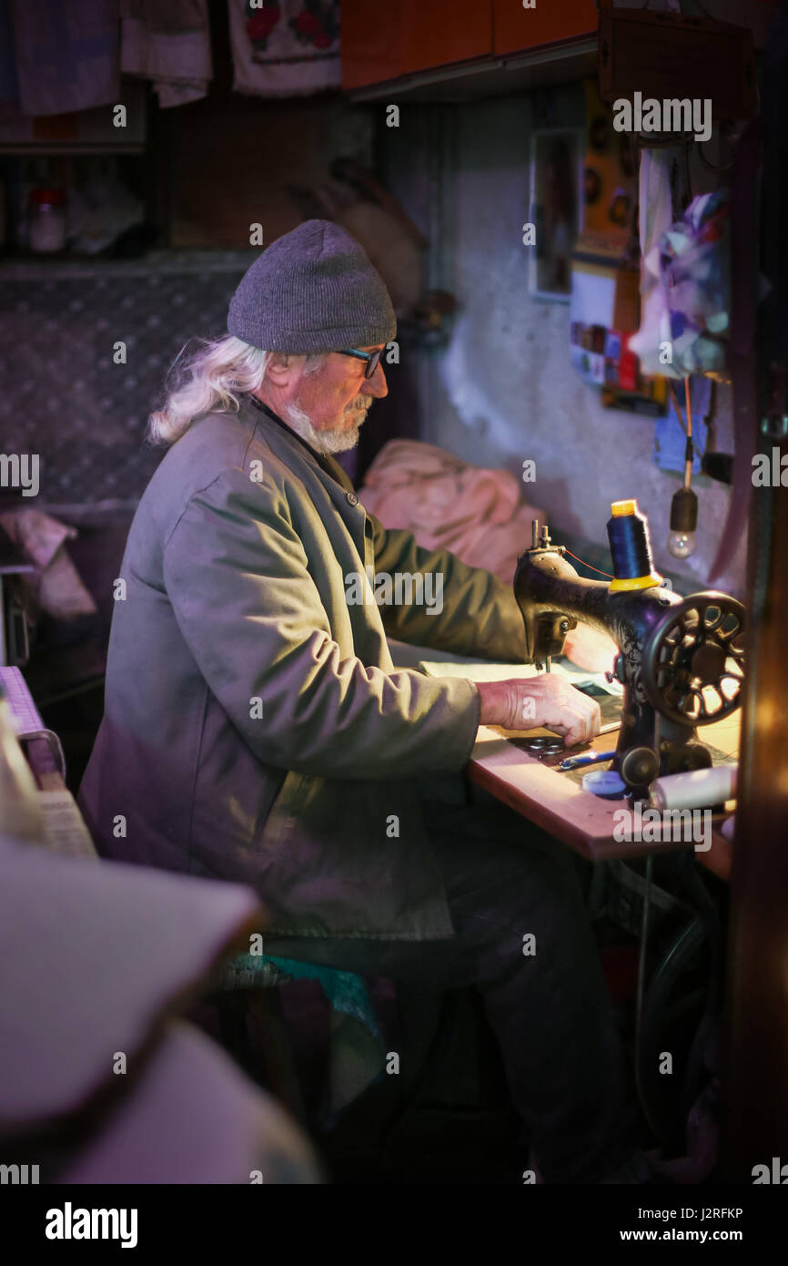 Un hombre adulto senior coser un pedazo de tela de una máquina de coser. Foto de stock