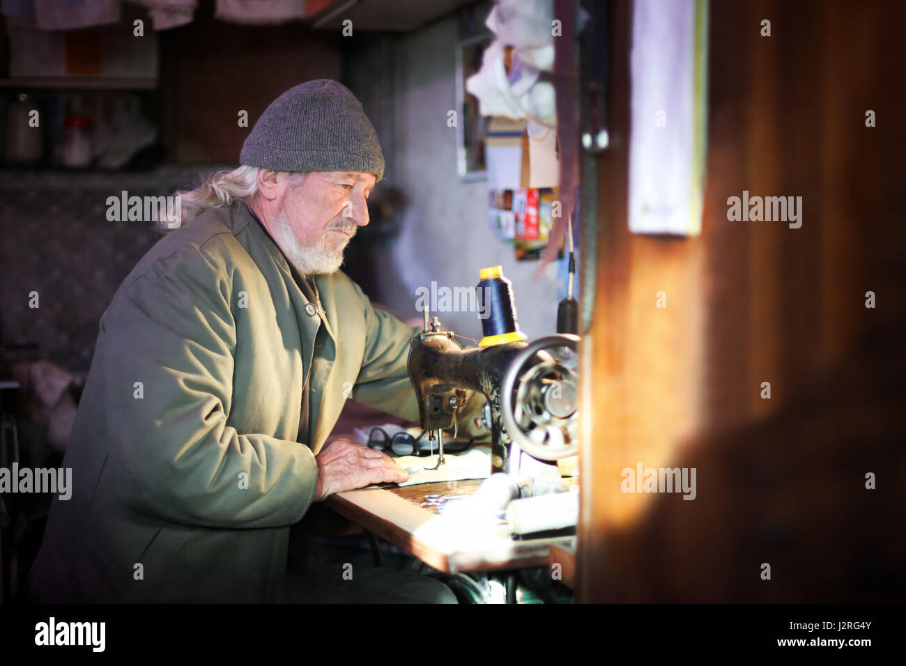 Un hombre adulto senior coser un pedazo de tela de una máquina de coser. Foto de stock