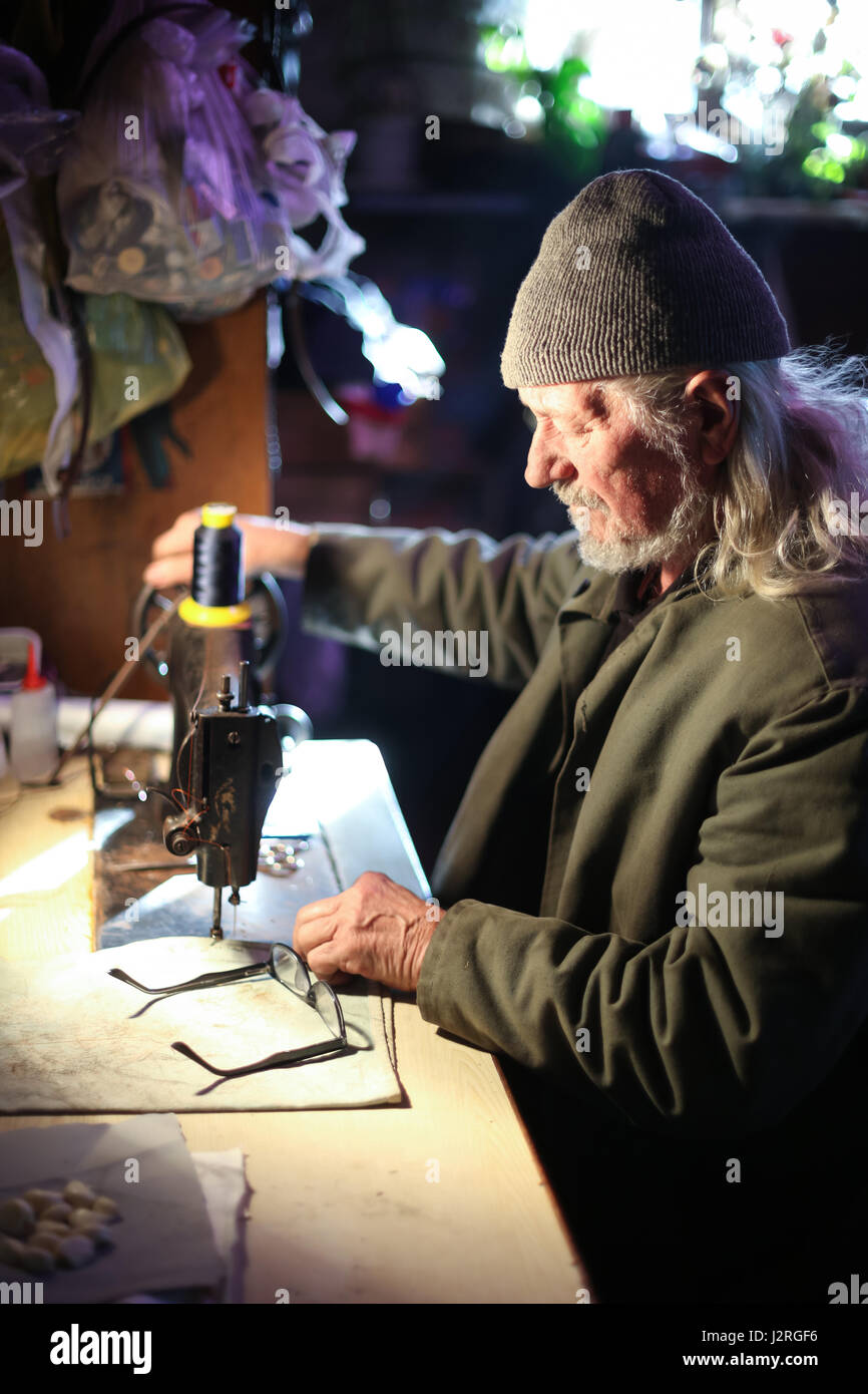 Un hombre adulto senior coser un pedazo de tela de una máquina de coser. Foto de stock