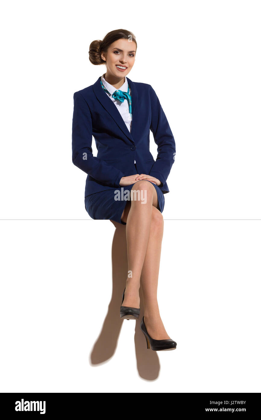 Mujer elegante azul traje, falda y zapatos de tacón negro, sentado en un comienzo con las piernas cruzadas, sonriendo y mirando a la cámara. Foto de estudio de longitud completa Fotografía