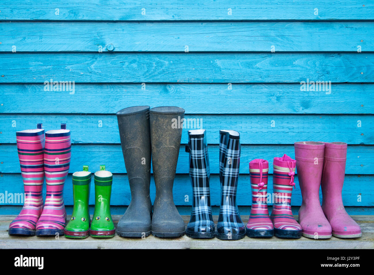 Muchas botas de goma de colores frente a una pared de madera azul  Fotografía de stock - Alamy