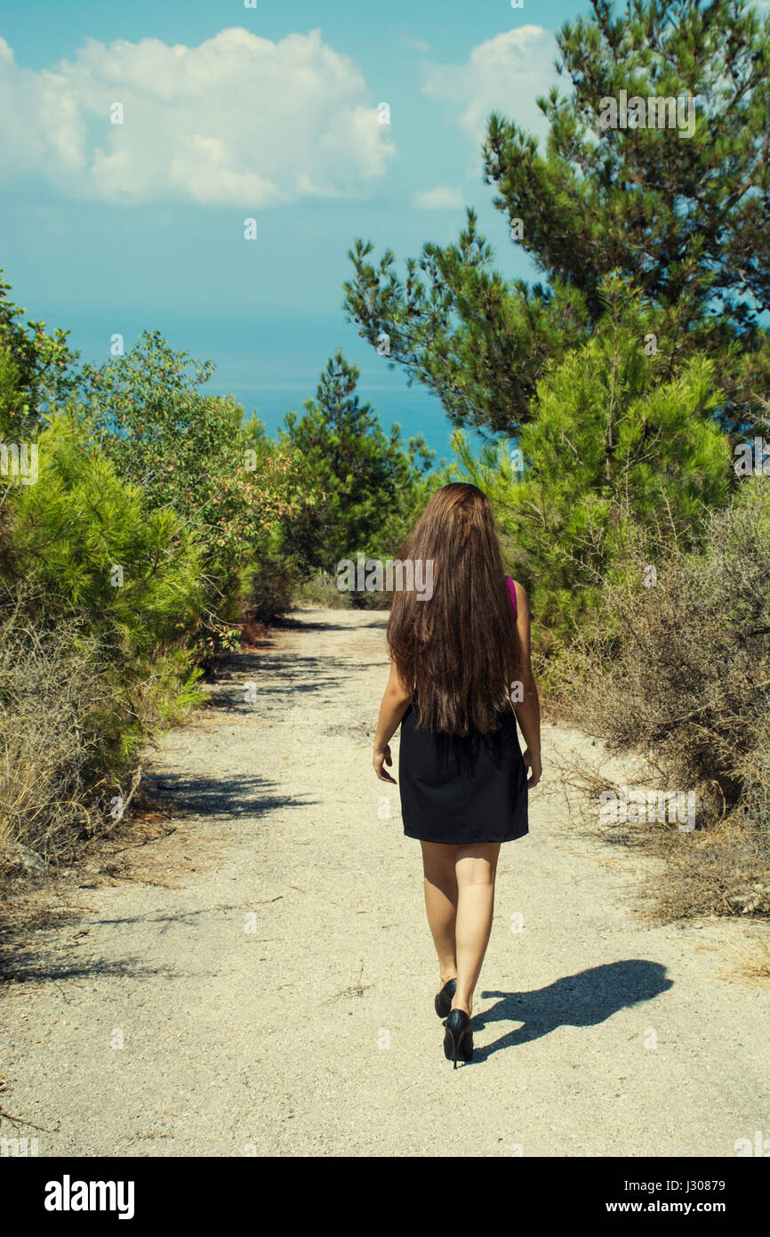 Vista trasera de la longitud completa de una mujer joven caminando en una carretera rural Foto de stock