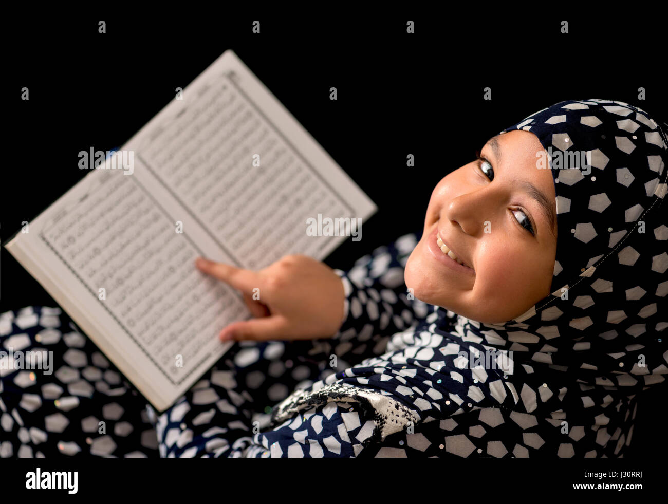 Chica musulmana leyendo el Corán sobre fondo negro Foto de stock