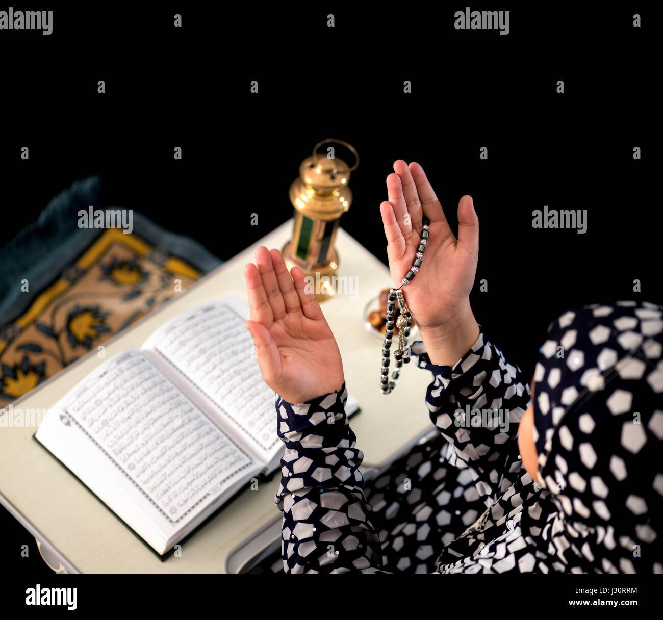 Chica musulmana levantando las manos para la oración sobre fondo negro Foto de stock
