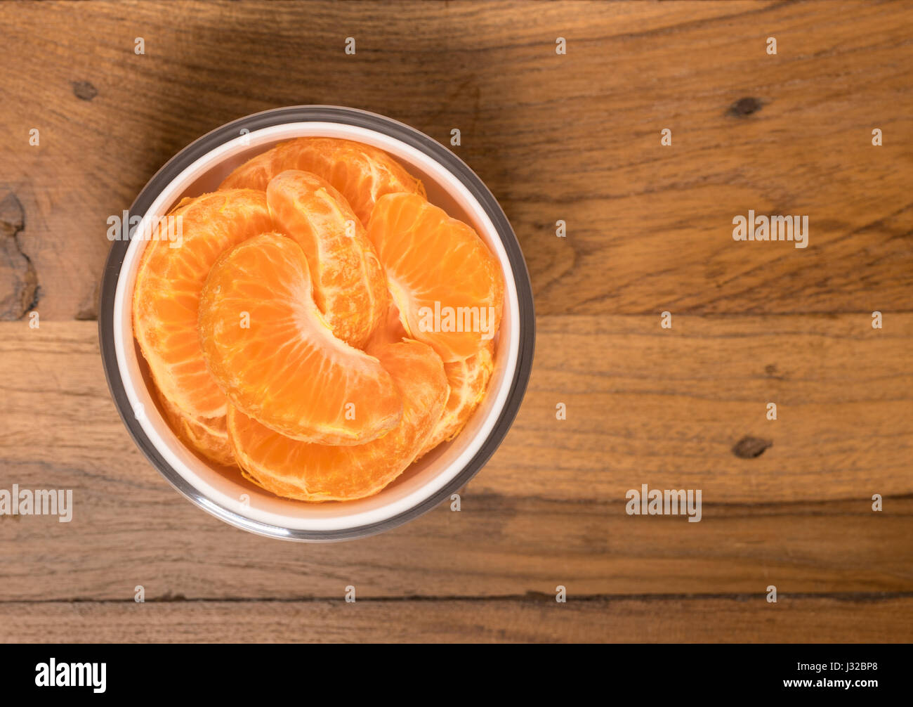 Rodajas de naranja o de mandarina en un recipiente sobre una mesa de madera de superficie Foto de stock