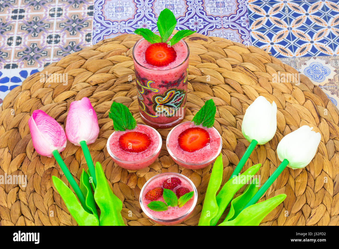 Una taza de jugo de fresas con hojas de menta sobre un fondo de colores orientales / taza de jugo de fresas sobre un fondo de colores orientales con flor Foto de stock
