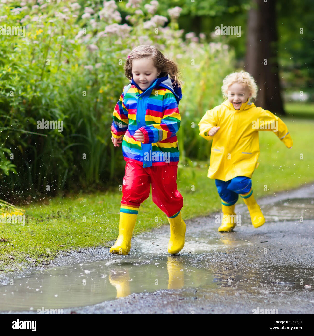 Niño con capa impermeable amarilla y botas de goma negras de pie en un  charco al aire libre bajo la lluvia en otoño.