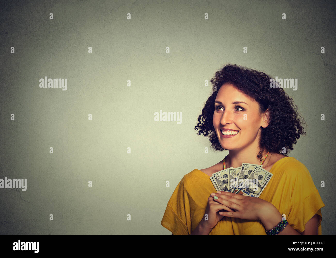 Closeup retrato feliz emocionado exitosa mujer de negocios jóvenes sosteniendo dinero billetes de dólar en mano buscando aislarse pared gris de fondo. E positivo Foto de stock
