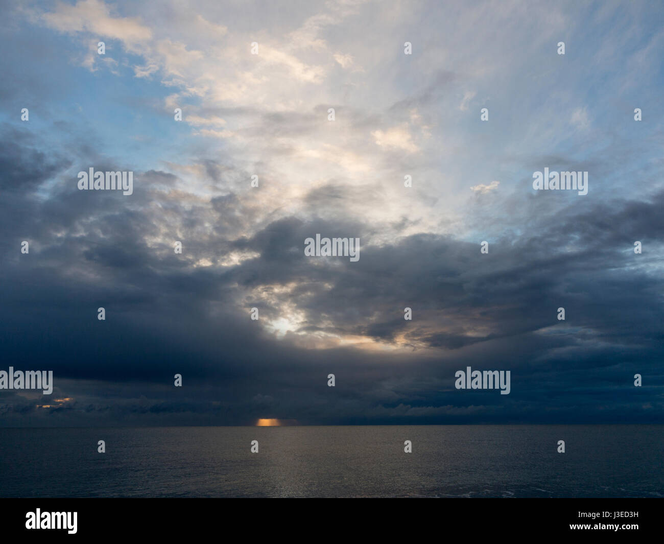 Amanecer detrás de Dark enojado nubes sobre el horizonte del mar del Norte la creación de un hot spot de luz naranja Foto de stock