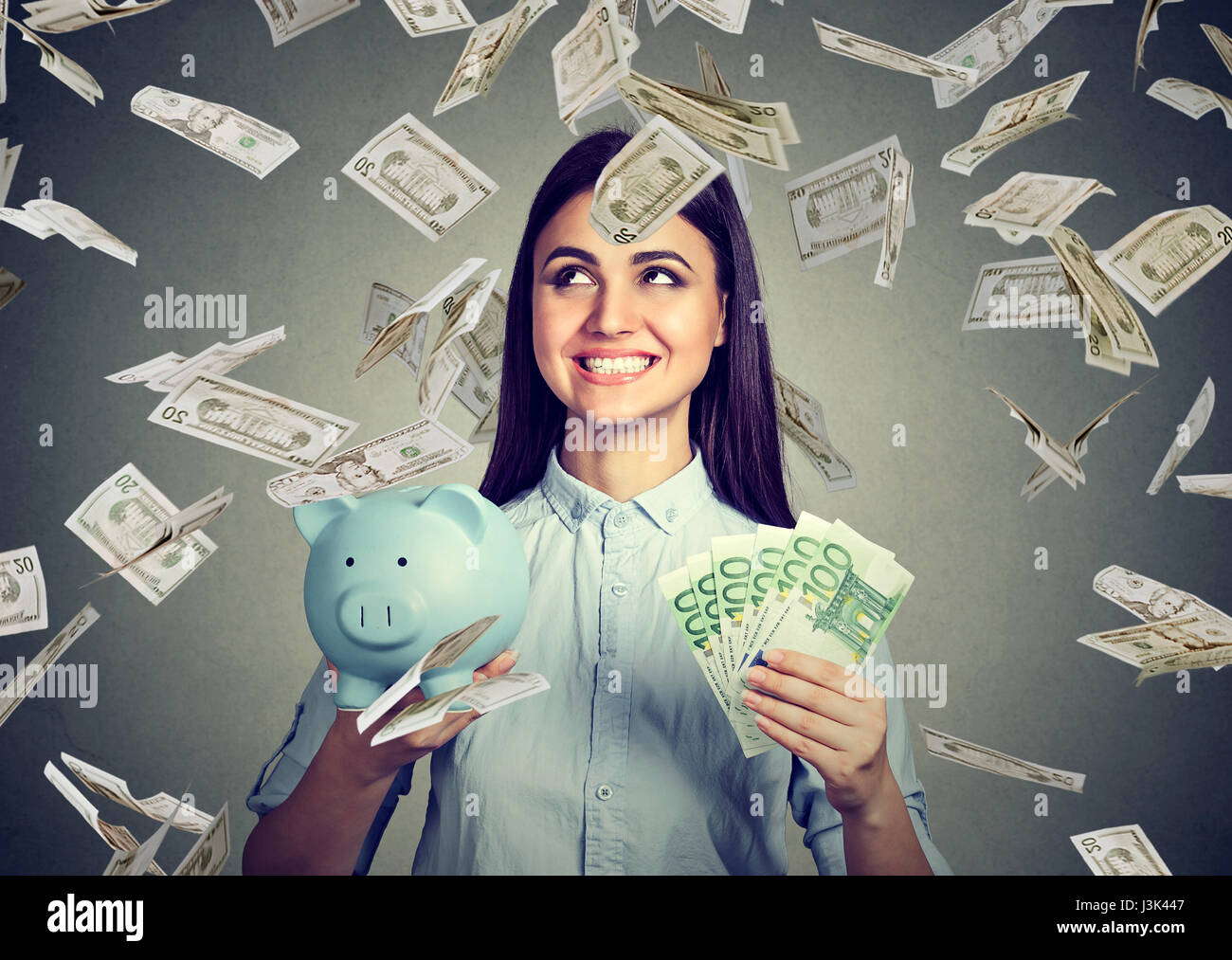 Mujer joven con alcancía y euro dólar dinero efectivo bajo la lluvia Foto de stock