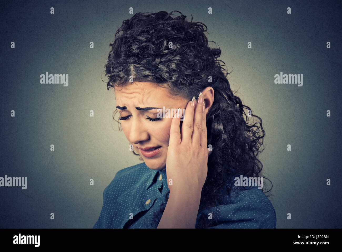 El Tinnitus. Closeup retrato de perfil del lado femenino enfermo tener dolor de oído tocar su cabeza dolorosa aislado sobre fondo de pared gris Foto de stock