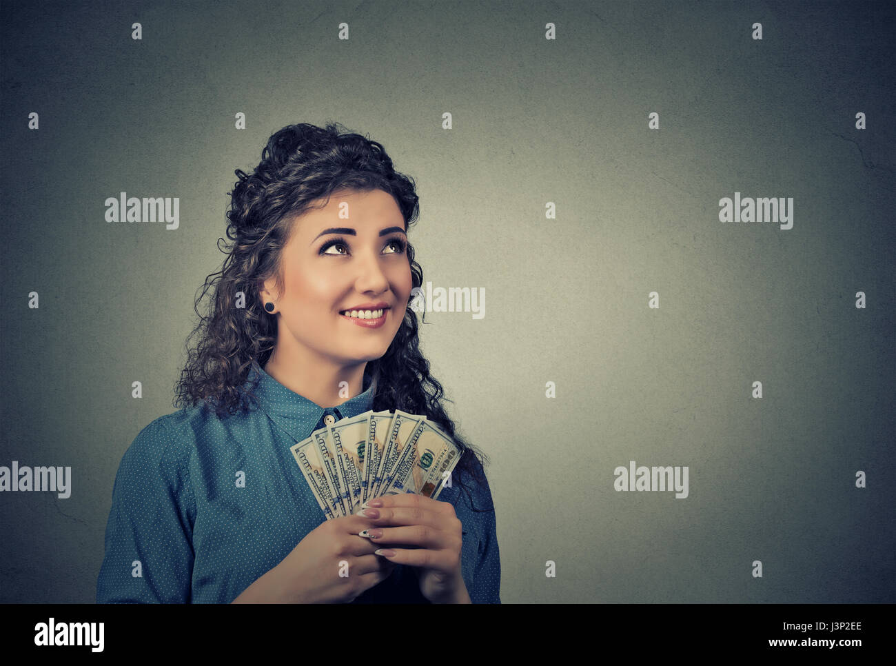 Closeup retrato feliz emocionado exitosa mujer de negocios jóvenes sosteniendo dinero billetes de dólar en mano buscando aislarse pared gris de fondo. E positivo Foto de stock