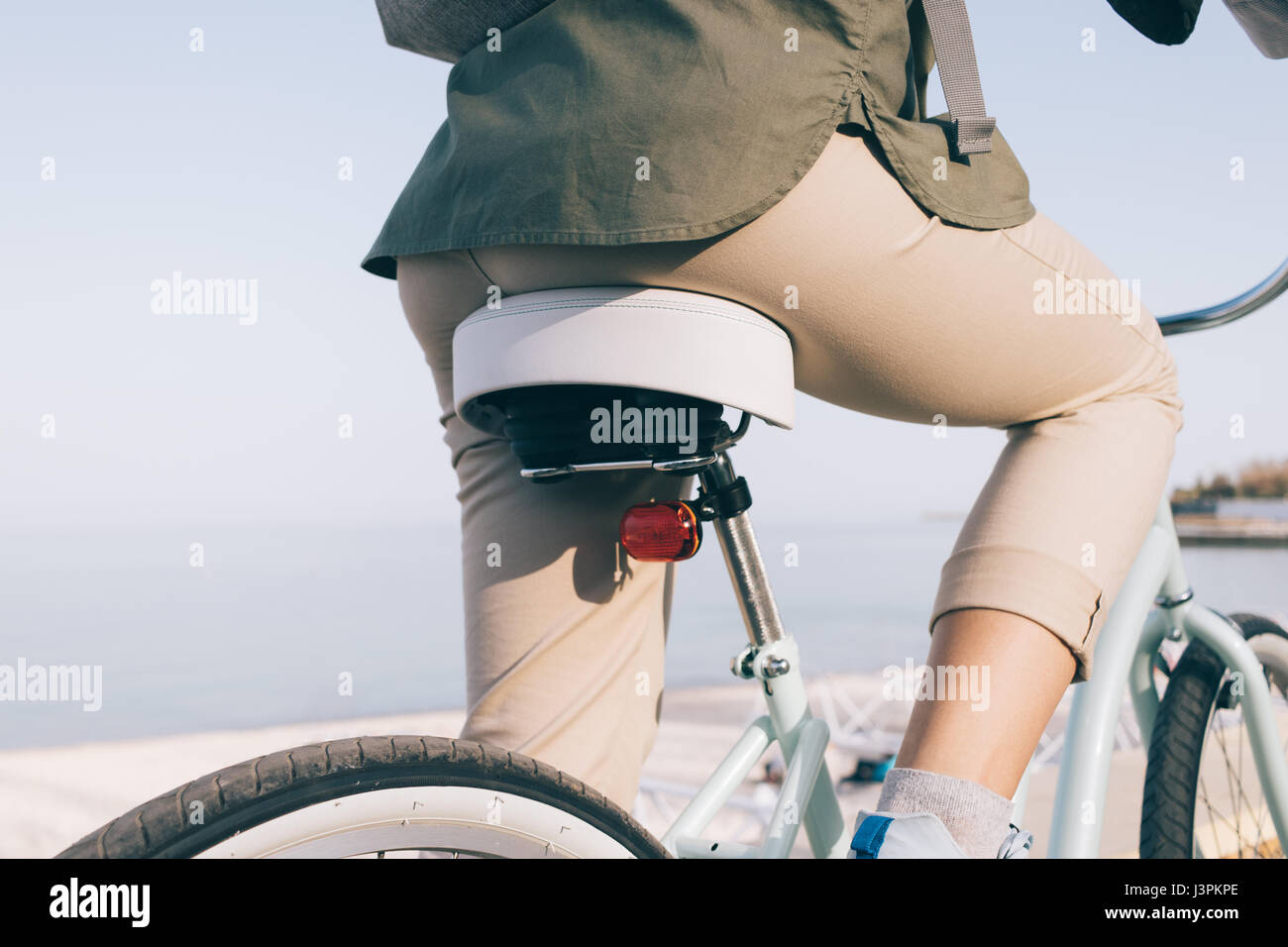 Primer plano de una esbelta chica en beige de pantalones y una camisa verde  sentado en una bicicleta en la playa frente al mar, vista trasera  Fotografía de stock - Alamy