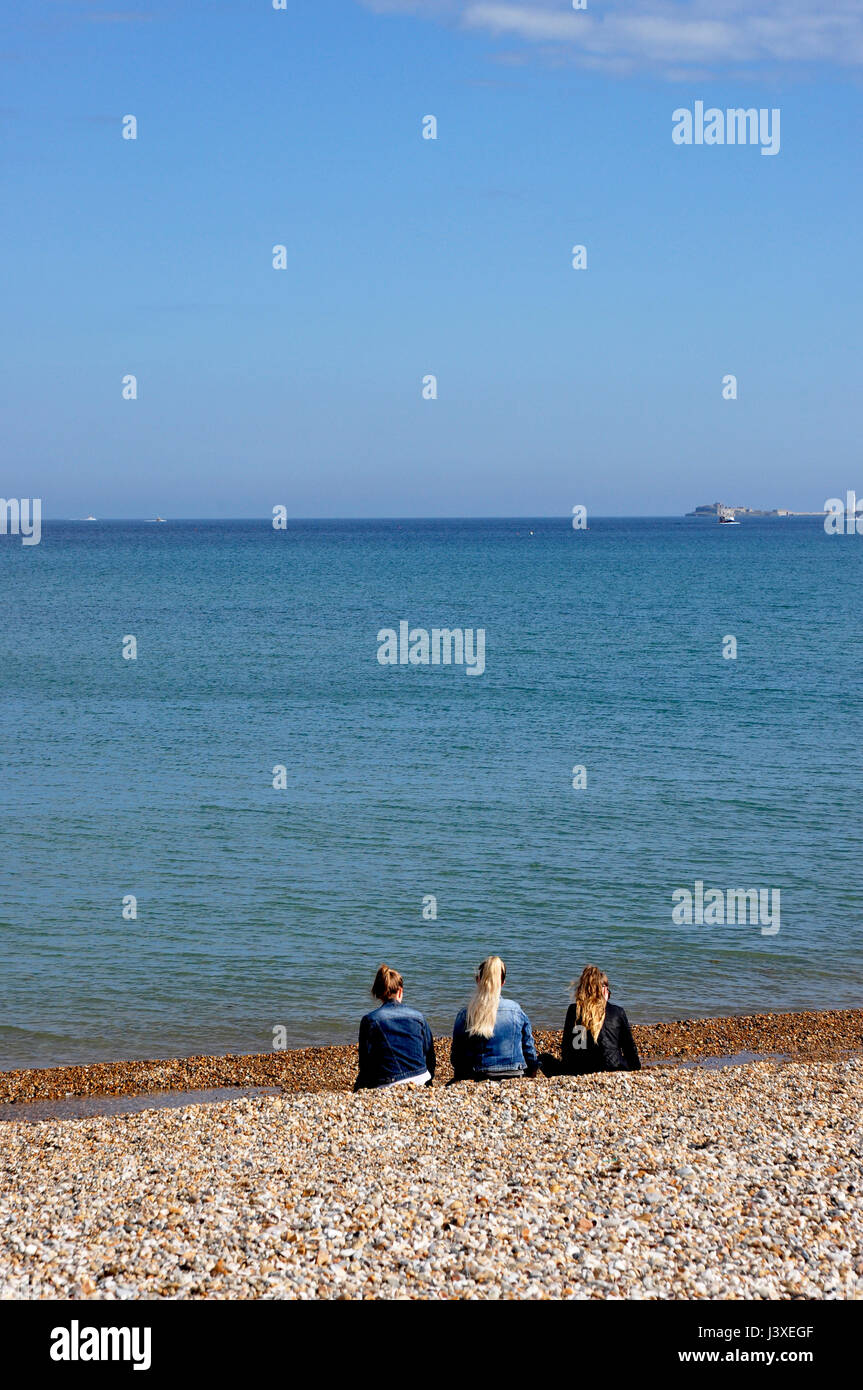 Tres niñas sentados en una playa mirando al mar - guijarros azul del cielo y del mar - barco en el horizonte - ilusiones - la imaginación en el trabajo - la luz del sol Foto de stock