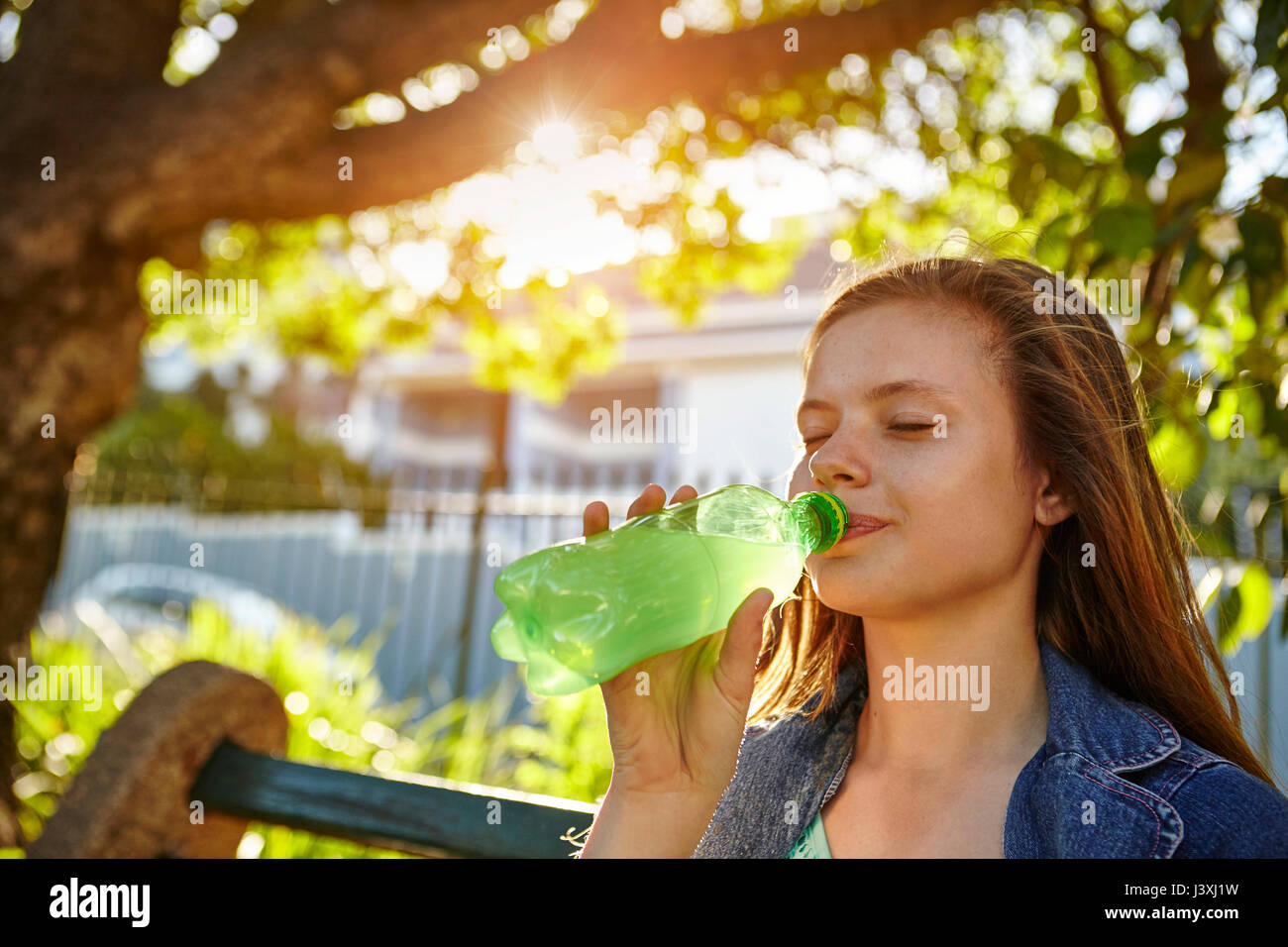 Adolescente, sentado en un banco, beber un refresco de botella