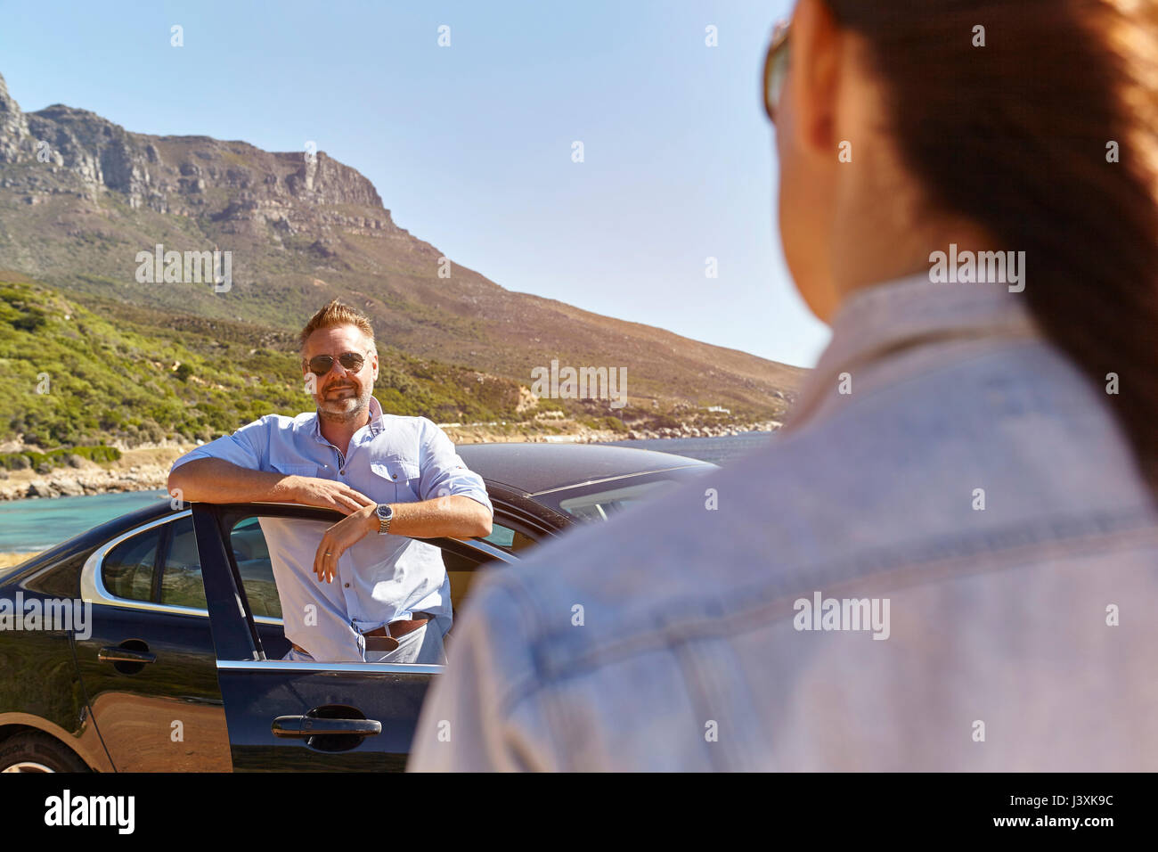 Hombre de pie por abrir la puerta de coche, mujer caminando hacia él Foto de stock