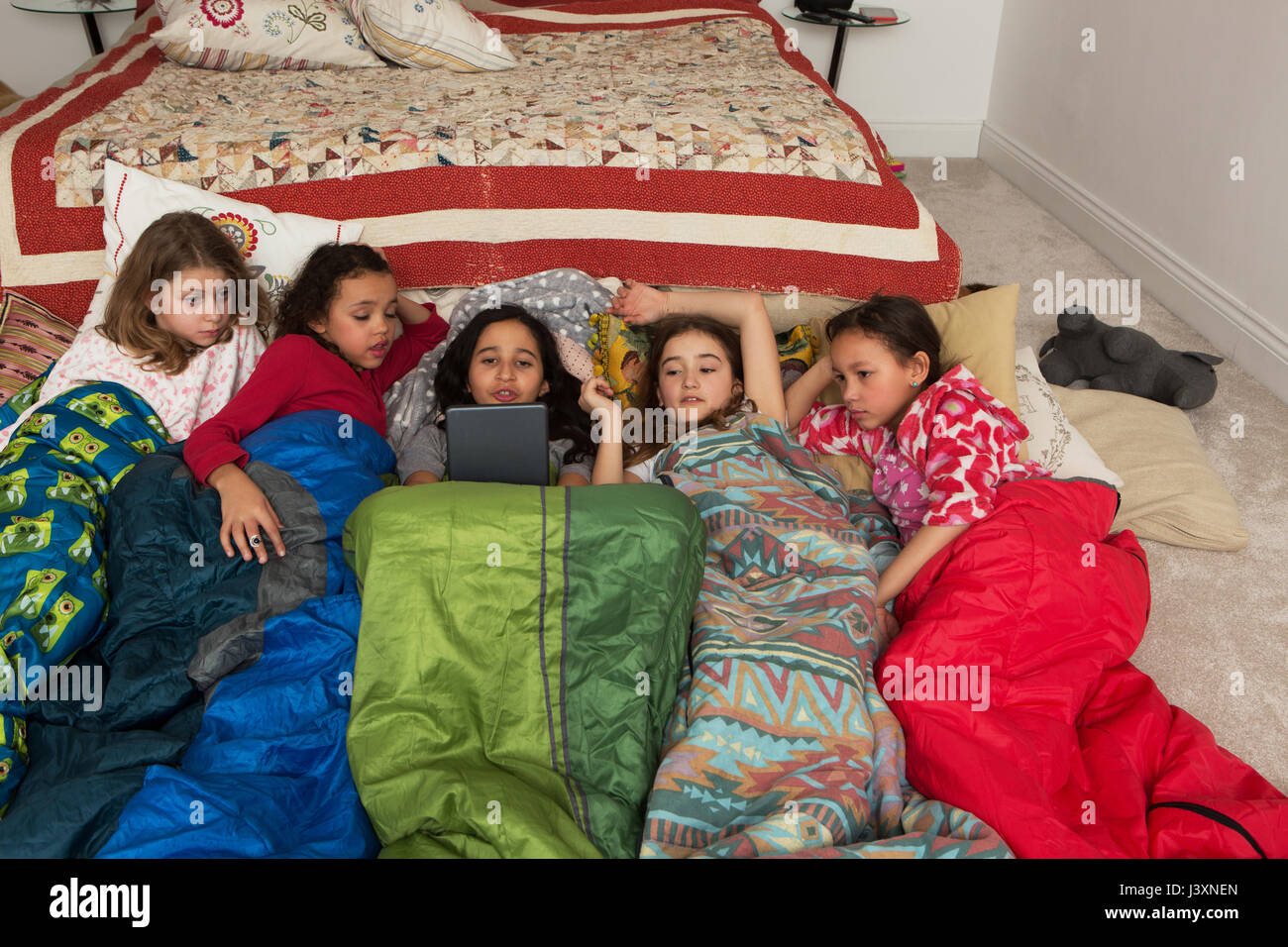Las niñas en sacos de dormir en Slumber Party mediante tableta digital Foto de stock