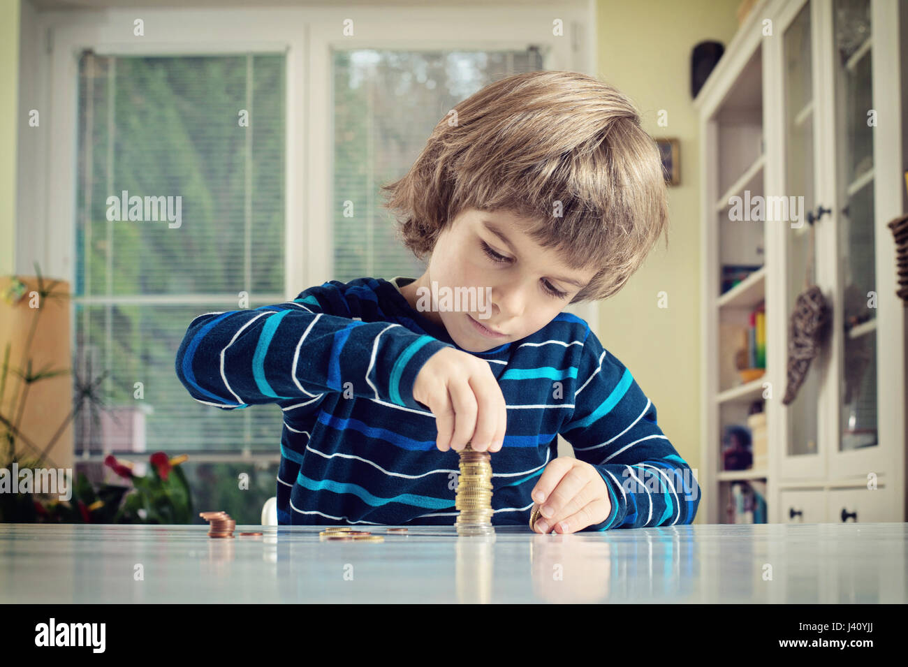 Little Boy haciendo pila de monedas, contando el dinero en la mesa. El aprendizaje la responsabilidad financiera y la planificación concepto de ahorro. Foto de stock