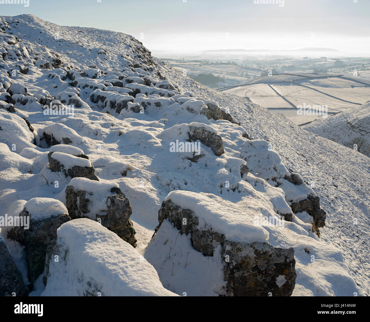 Nieve soleada sobre el pavimento de piedra caliza por encima de Malham, Yorkshire Dales. Vista sobre los campos nevados de Pendle en la distancia. Foco imagen de paisaje apiladas. Foto de stock