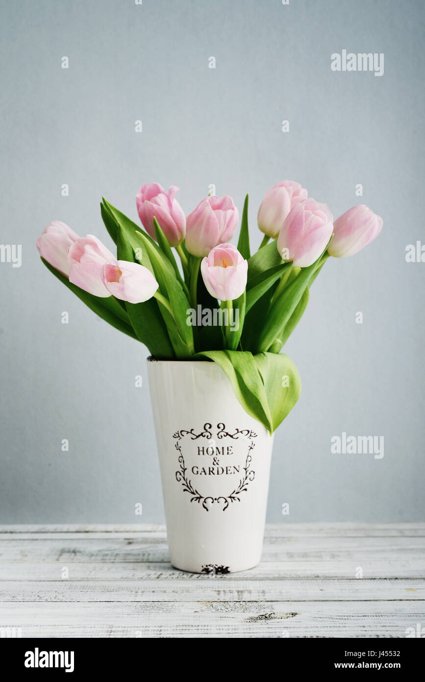 Ramo de tulipanes rosa en un jarrón sobre fondo azul. Foto de stock