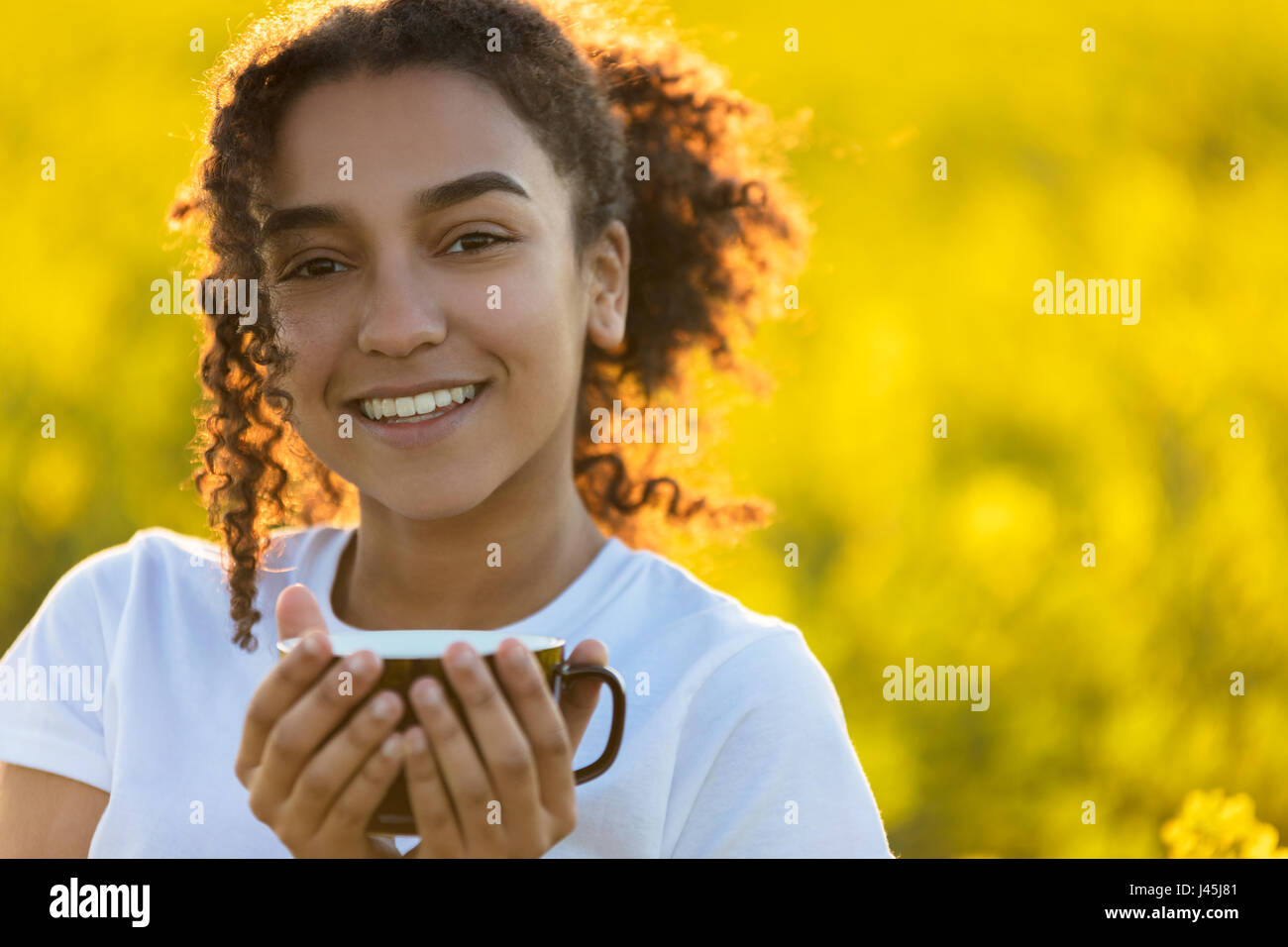 Feliz hermosa chica americana africana de raza mixta femenina adolescente joven sonriente bebiendo té o café al aire libre Foto de stock