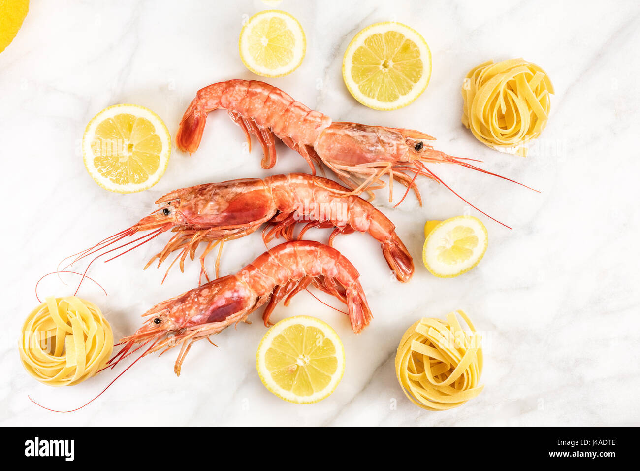 Camarones crudos con limón y pasta sobre la mesa de mármol Foto de stock
