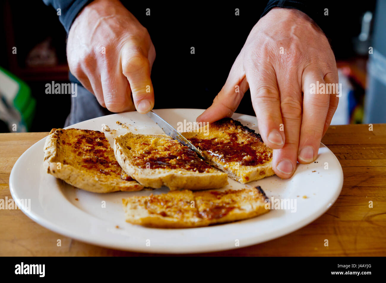 Vista cercana del hombre cortando un trozo de pan tostado en una placa blanca. Foto de stock