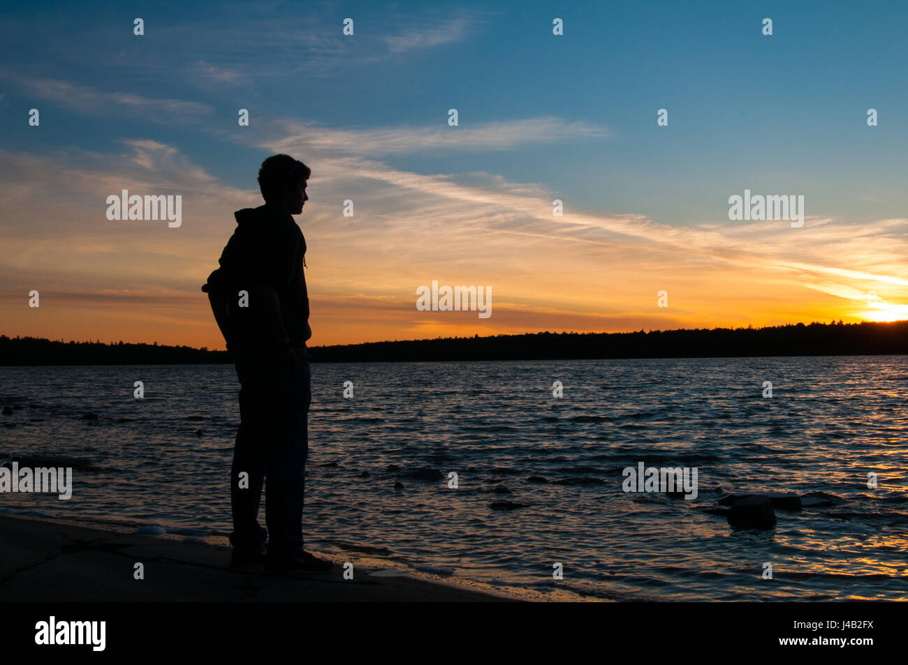 Adolescente mira el sol sobre un lago Foto de stock