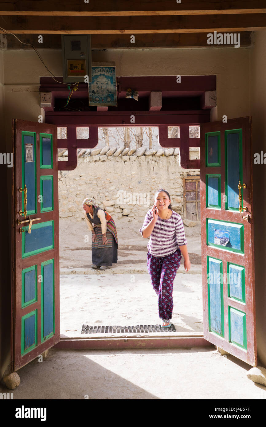 Chica adolescente habla Tibetano en el teléfono celular y la mujer de edad, vestidos con ropas tradicionales en el fondo. Foto de stock