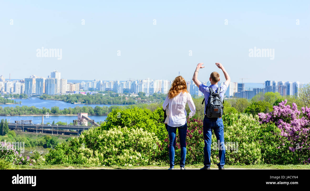 Los jóvenes feliz costes sobre la colina en el soleado día de verano y mira un panorama de la gran ciudad Foto de stock