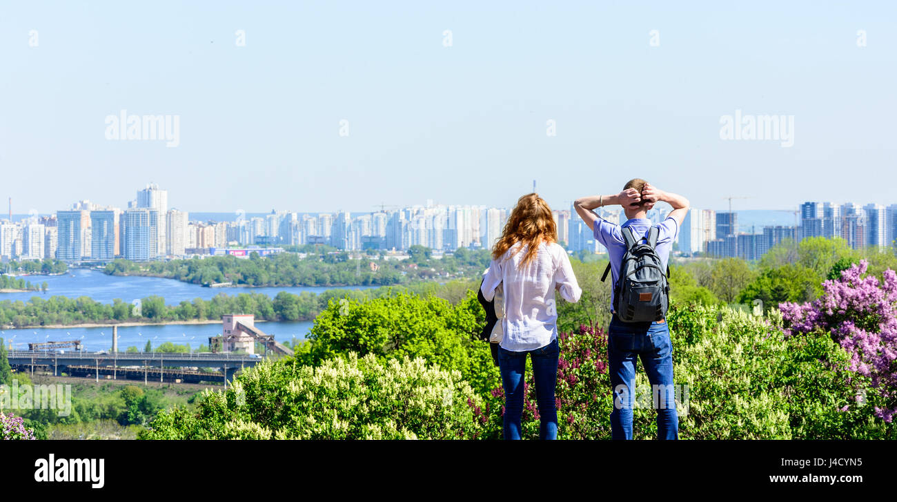 Los jóvenes feliz costes sobre la colina en el soleado día de verano y mira un panorama de la gran ciudad Foto de stock