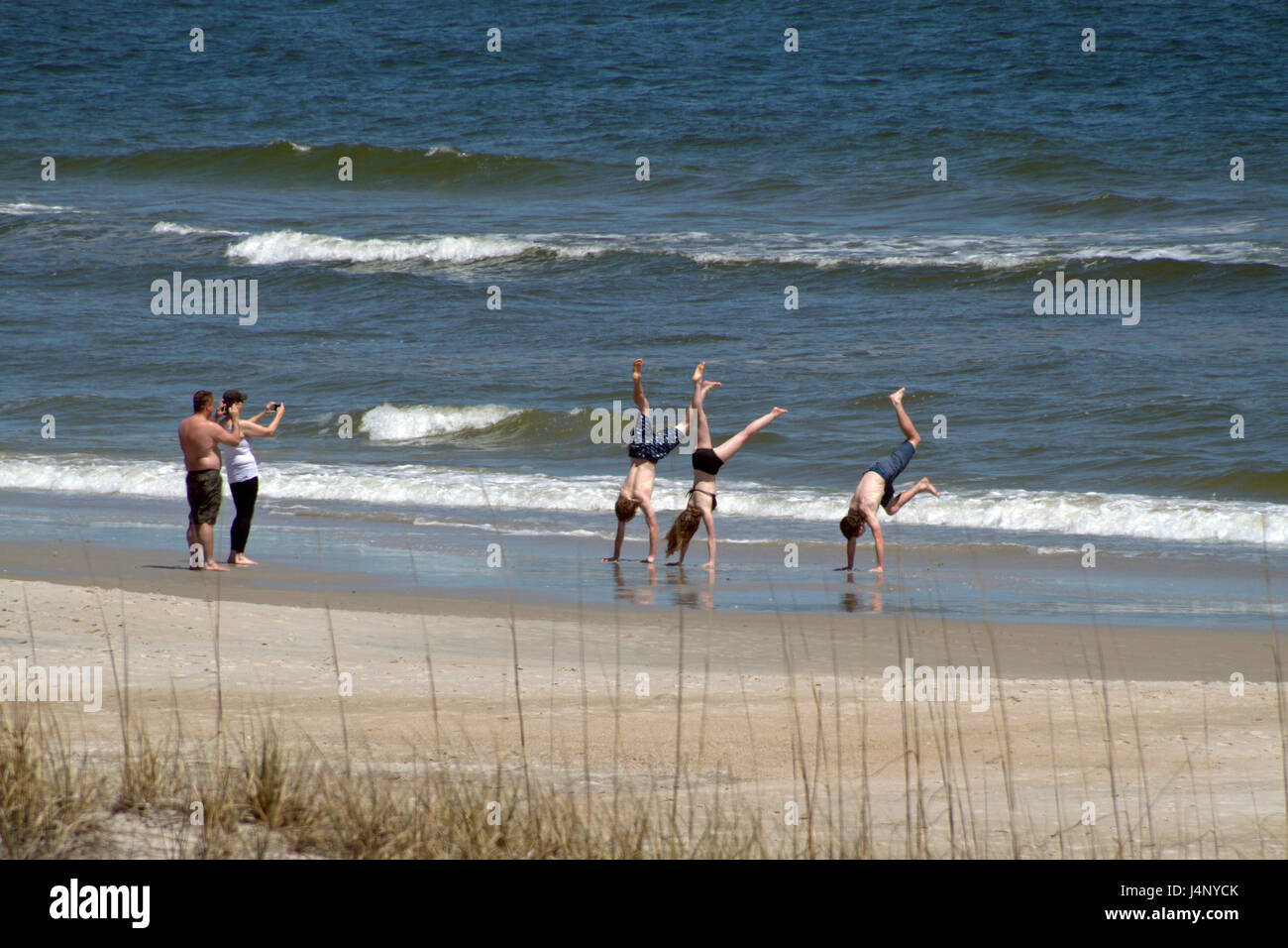 Carolina Beach, Carolina del Norte, EE.UU. - 11 de abril de 2017: tres jóvenes ¿athletic handstands en el agua de mar la marea entrante en una playa soleada Foto de stock