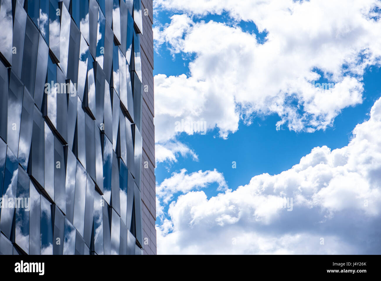 Reflexiones de cielo nublado en un futurista edificio moderno con fachada de cristal para fines terciarios, rascacielos en un distrito financiero, detalles Foto de stock