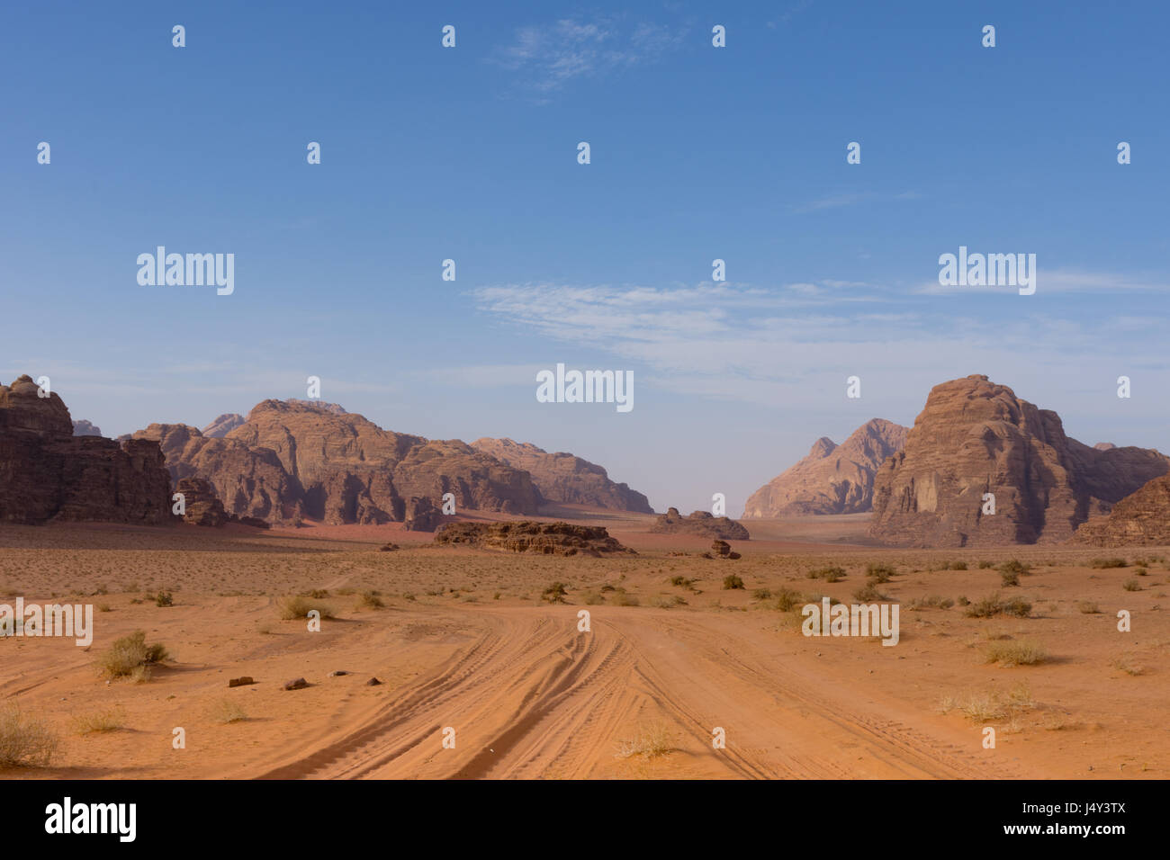 Vehículos de cuatro ruedas carretera a través de orange u óxido arena coloreada con montañas en la distancia con el azul intenso del cielo arriba. Fotografiado en Wadi Rum Desert Foto de stock